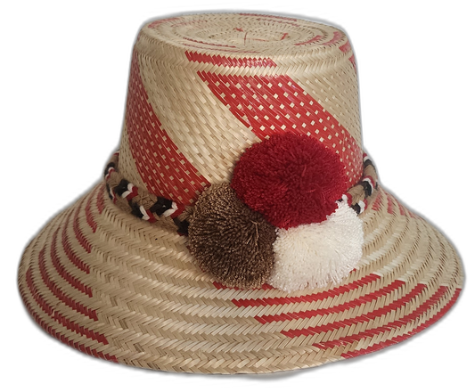 Handmade Wayuu straw hat featuring bold red patterns, with decorative white, brown, and red pompoms.