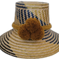 Handmade Wayuu straw hat with golden-brown pompoms and navy blue chevron weave.Boho straw hat in natural and dark blue tones with artisan pompoms

