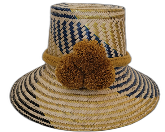 Handmade Wayuu straw hat with golden-brown pompoms and navy blue chevron weave.Boho straw hat in natural and dark blue tones with artisan pompoms