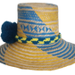 Colorful Wayuu hat in yellow and blue spiral pattern, with artisan pompom detail