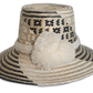 Handmade Wayuu boho straw hat with black and natural geometric weaving and ivory pompoms.