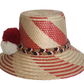 Boho chick hat woven from Iraca palm with red diagonal accents and pompom trim handmade by Wayuu artisans.