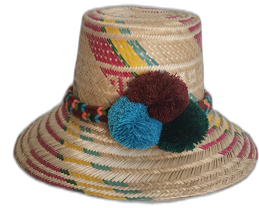 Handmade Wayuu straw hat with red, yellow, and green weaving, accented by large pompoms in brown, teal, and green.